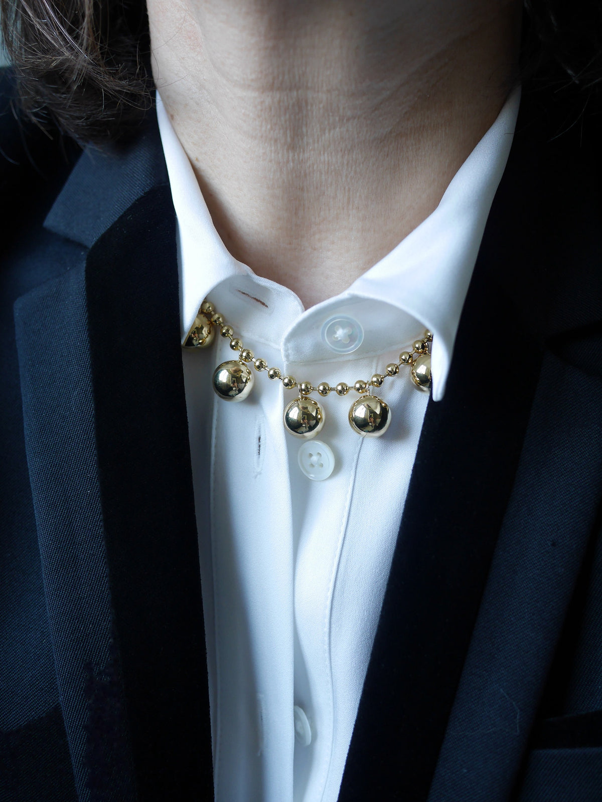Collier Sphère à boules dorées porté sur une chemise blanche avec un blazer sombre