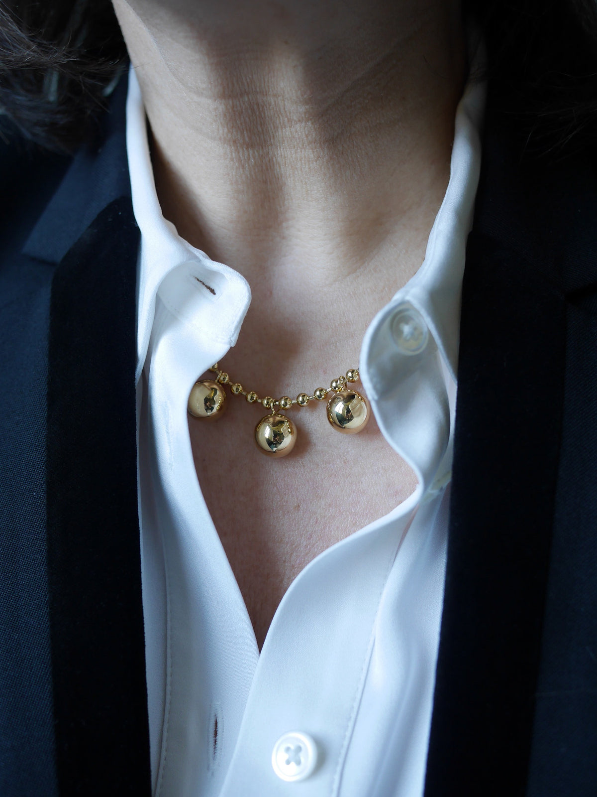 Collier Sphère à pampilles boules dorées porté au creux d’un col de chemise ouvert